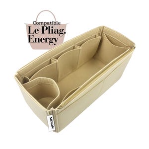 May include: Beige felt bag organizer with multiple compartments and a gold zipper. The organizer is designed to fit inside a handbag. The text "Compatible Le Pliag. Energy" is in the upper left corner. The brand name "SILKON" is on a white tag.