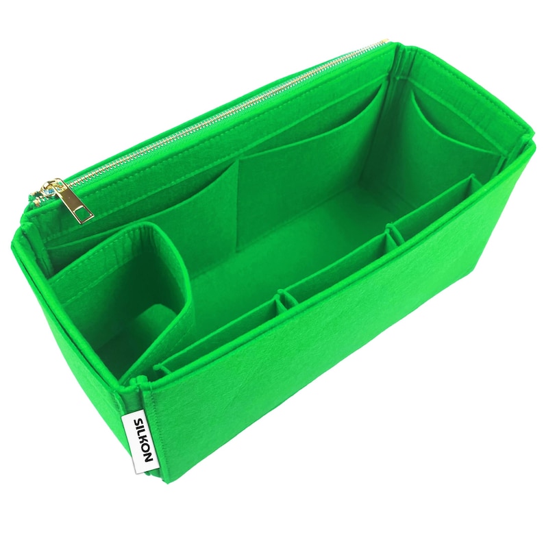 May include: Bright green felt bag organizer with multiple compartments and a gold zipper. The organizer has several pockets of varying sizes and a label that reads "SILKON". This item is designed to help organize the contents of a handbag.