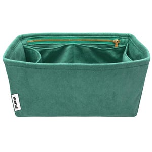 May include: A teal handbag organiser with several compartments and a zipped top. The organiser is made of a soft, suede-like material and features a gold-coloured zip and the brand name "SILKON" on a white label.