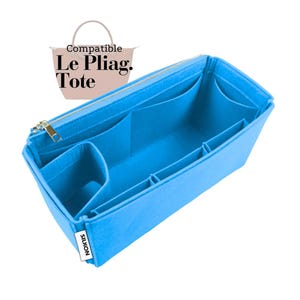 Puede incluir: Un organizador de bolso tote de color azul brillante con múltiples compartimentos y un cierre de cremallera. El organizador está diseñado para encajar dentro de un bolso Le Pliag. Tote. La palabra "SILKON" está impresa en una pequeña etiqueta blanca en el lateral.