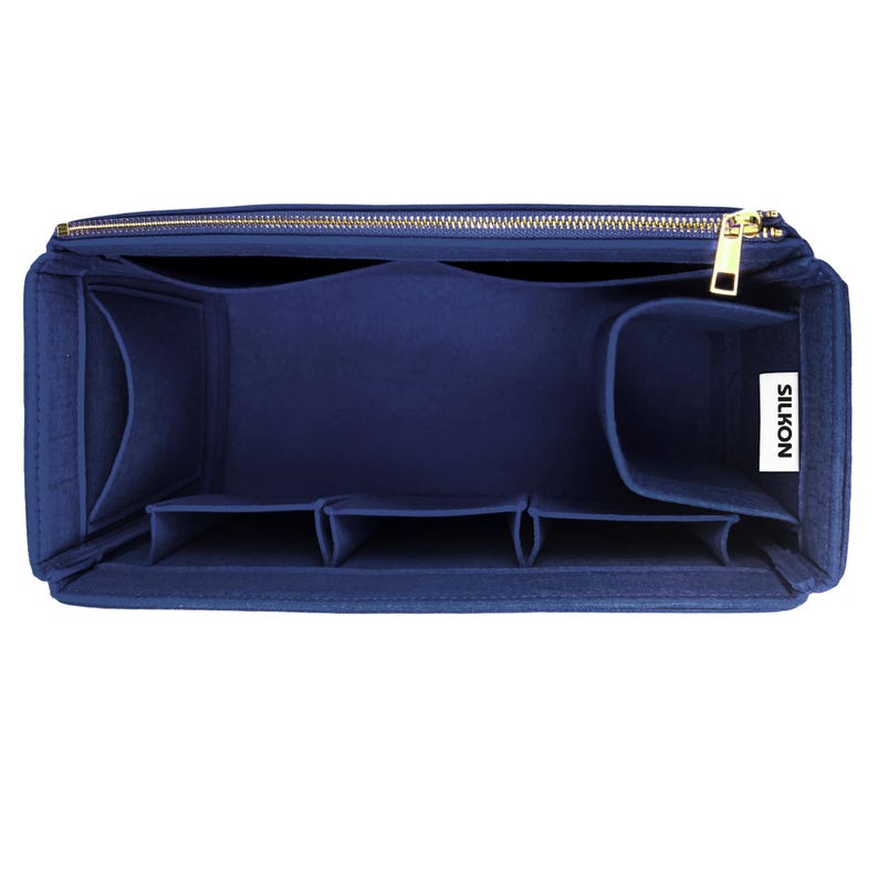 May include: A navy blue felt bag organizer with multiple compartments and a gold zipper. The organizer has a rectangular shape and is designed to fit inside a larger bag. The brand name "SILKON" is visible on a white tag.