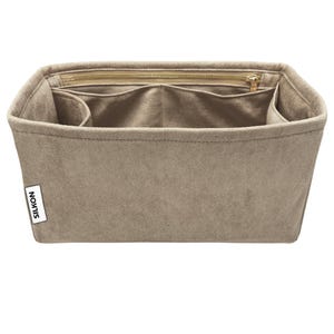 May include: A beige handbag organizer with multiple compartments and a zippered top closure. The organizer has a rectangular shape and a soft, suede-like texture. The brand name "SILKON" is visible on a small white tag.