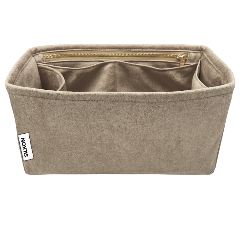 May include: A beige handbag organizer with multiple compartments and a zippered top closure. The organizer has a rectangular shape and a soft, suede-like texture. The brand name "SILKON" is visible on a small white tag.