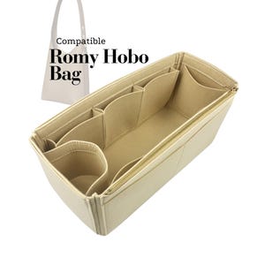 May include: Beige bag organizer with multiple compartments and a gold zipper. The text "Compatible Romy Hobo Bag" is printed on the upper left. The organizer is designed to fit inside a handbag, providing structure and organization.