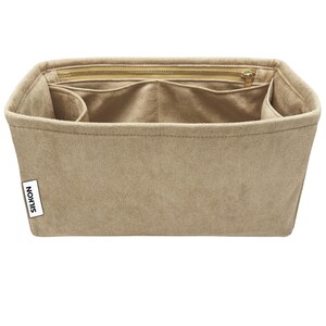 May include: Beige handbag organizer with multiple compartments and a zippered top. The organizer is made of a soft, suede-like material and features the brand name "SILKON" on a small white tag.