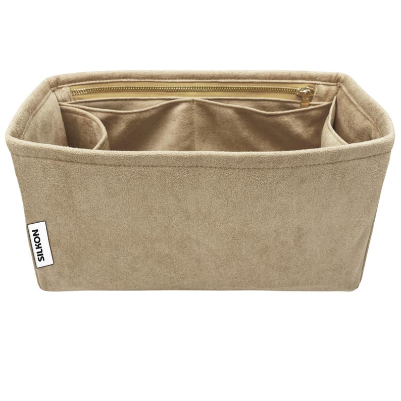 May include: Beige handbag organizer with multiple compartments and a zippered top. The organizer is made of a soft, suede-like material and features the brand name "SILKON" on a small white tag.