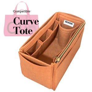 Può includere: Un organizer per borsa rettangolare in feltro arancione con molteplici scomparti interni, una tasca cilindrica e una chiusura a zip dorata. Un'etichetta bianca con il testo SILKON è fissata all'interno. Un grafico rosa mostra il testo Compatible Curve Tote.