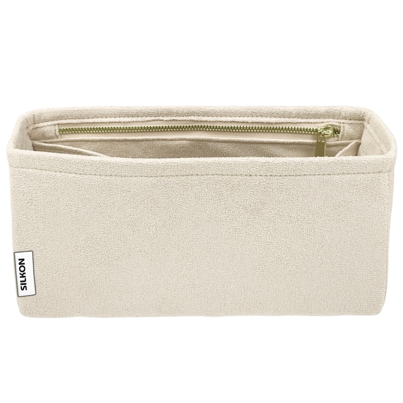 May include: Beige rectangular bag organizer with a zippered top and multiple compartments. The bag is made of a soft, textured material and features a gold-colored zipper. The brand name "SILKON" is printed on a small label on the side.