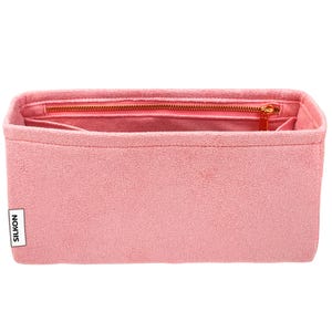 May include: A pink bag organizer with a zippered top and multiple interior pockets. The organizer has a rectangular shape and a textured surface. The zipper and zipper pull are gold-colored. The brand name "SILKON" is printed on a white label.