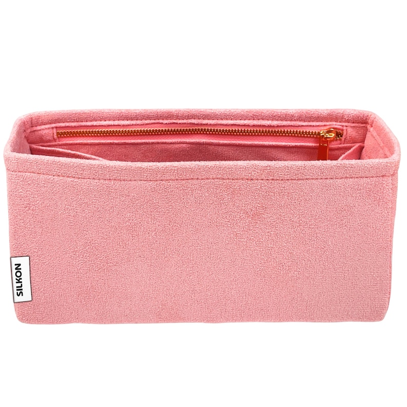 May include: A pink bag organizer with a zippered top and multiple interior pockets. The organizer has a rectangular shape and a textured surface. The zipper and zipper pull are gold-colored. The brand name "SILKON" is printed on a white label.
