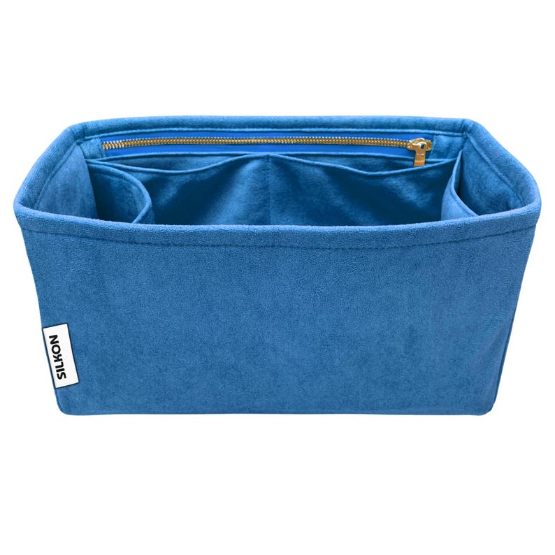 May include: A blue felt bag organizer with multiple compartments and a zippered pocket. The organizer has a rectangular shape with a structured design. The brand name "SILKON" is printed on a white label on the side. The zipper is gold-colored.