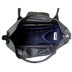 Puede incluir: Un bolso tote de color verde azulado oscuro con un inserto organizador de fieltro azul marino. El bolso tiene cierre de cremallera, asas de cuero negro y una solapa con cierre de botón a presión. Se ve un portátil dentro del bolso. El texto "SILKON" es visible.