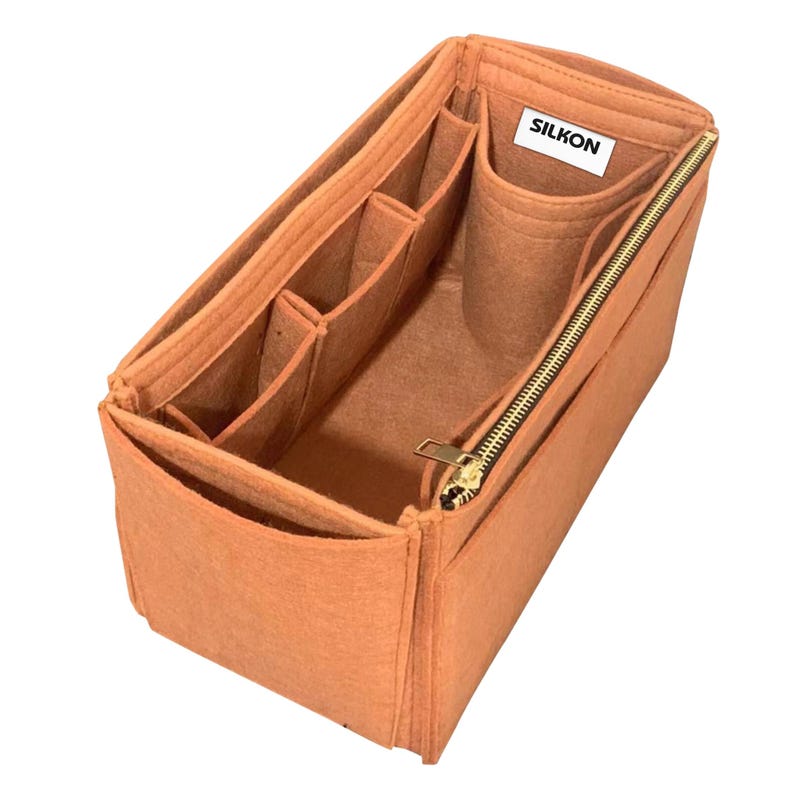 May include: A peach-colored felt bag organizer with multiple compartments and a zippered closure. The organizer has several pockets of varying sizes and a label that reads "SILKON". The zipper and zipper pull are gold-toned.