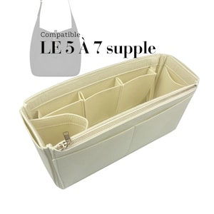 Puede incluir: Organizador de bolso de color crema con múltiples compartimentos y cierre de cremallera. El organizador está diseñado para caber dentro de un bolso más grande, con el texto "Compatible LE 5 À 7 supple" visible.