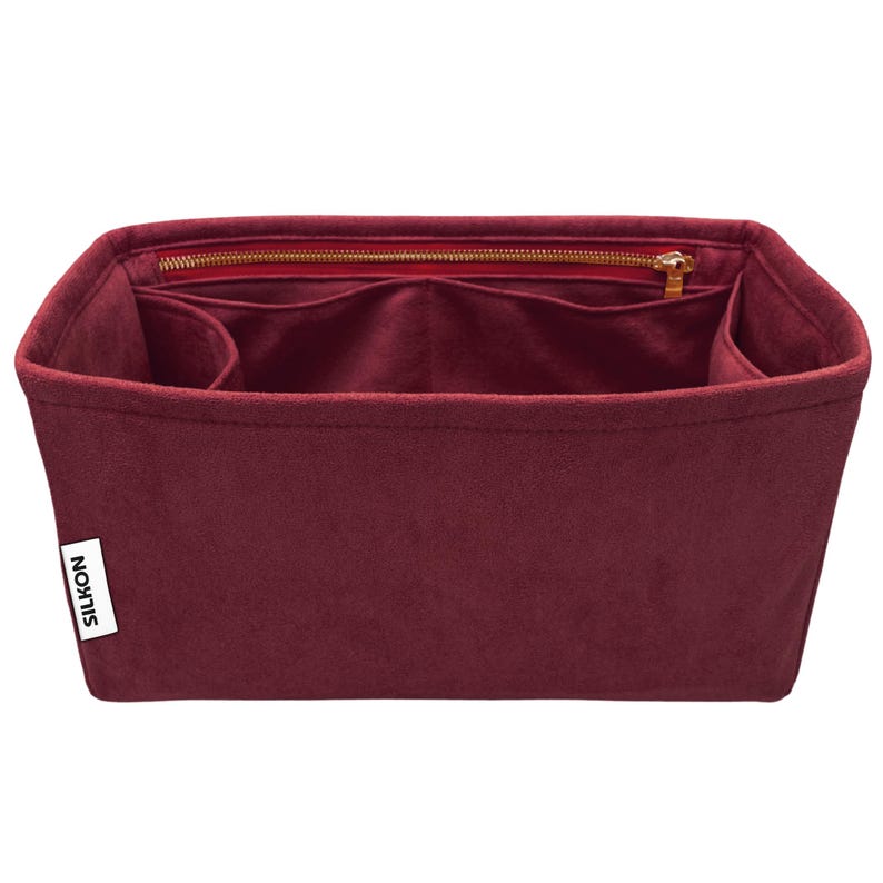 May include: A burgundy felt handbag organizer with multiple compartments and a zippered top closure. The organizer has a rectangular shape and a label that reads "SILKON". The interior features several pockets for organization.