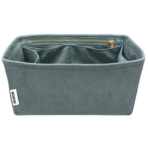 May include: A teal-colored bag organizer with multiple compartments and a zippered top closure. The organizer has a rectangular shape and is made of a soft, suede-like material. A white label with the word "SILKON" is visible on the side.