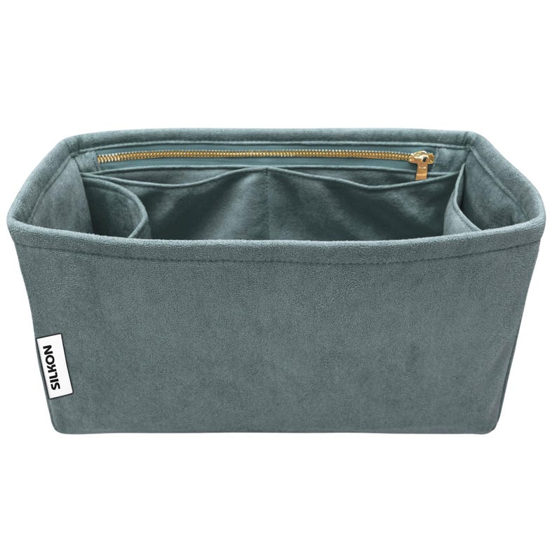 May include: A teal-colored bag organizer with multiple compartments and a zippered top closure. The organizer has a rectangular shape and is made of a soft, suede-like material. A white label with the word "SILKON" is visible on the side.