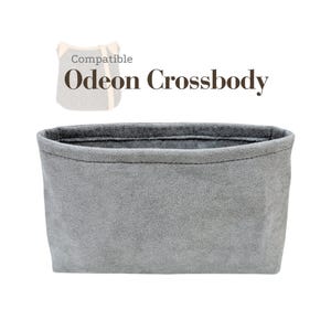 May include: A grey, rectangular tote bag with a soft, textured surface. The text "Compatible Odeon Crossbody" is displayed above the bag. The bag is designed to fit inside a crossbody bag.