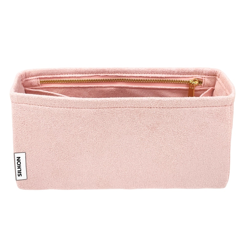 May include: A light pink handbag organizer with a zippered compartment and multiple pockets. The organizer has a rectangular shape and a gold-colored zipper. The brand name "SILKON" is printed on a white label on the side.
