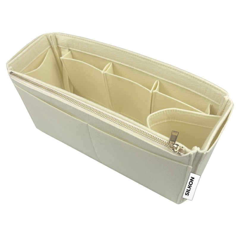 May include: Cream-colored felt bag organizer with multiple compartments and a zippered closure. The organizer has various pockets and sections for storing items. The "SILKON" brand label is visible on the side.