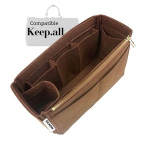 Puede incluir: Un organizador de bolso de fieltro marrón con múltiples compartimentos y una cremallera dorada. El organizador está diseñado para encajar dentro de un bolso Keep.all. Las palabras "Compatible" y "Keep.all" están impresas.
