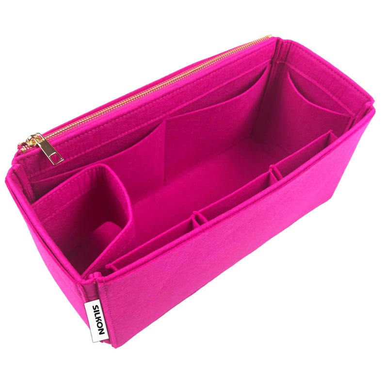May include: A bright pink felt bag organizer with multiple compartments and a gold zipper. The organizer has several pockets of varying sizes and a small label that reads "SILKON". The bag is designed to help organize items inside a larger bag.