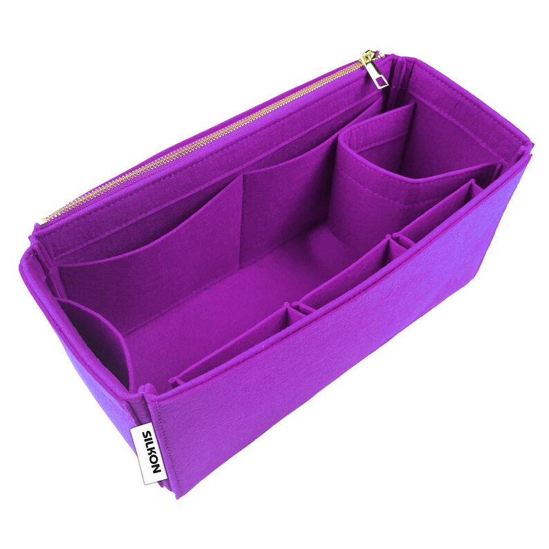 May include: A vibrant purple bag organizer with multiple compartments and a gold zipper. The organizer is made of felt and features various pockets and dividers for storage. The brand name "SILKON" is visible on a small white tag.