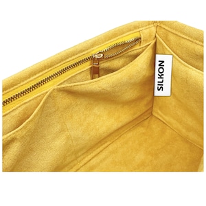 May include: Close-up of a yellow fabric organizer with multiple compartments and a gold zipper. The interior is a soft, velvety material. A white tag with the word "SILKON" is visible.