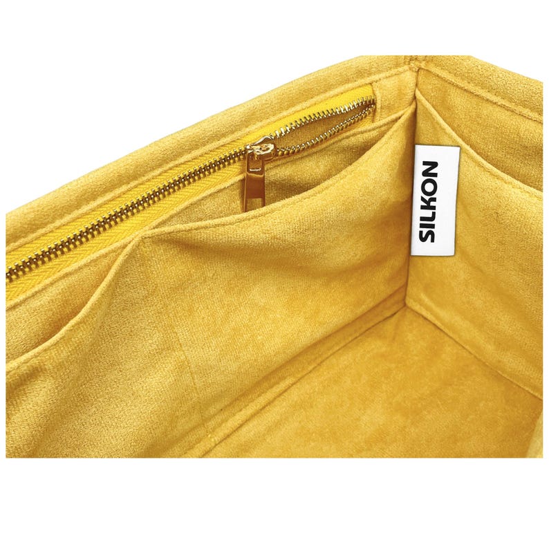 May include: Close-up of a yellow fabric organizer with multiple compartments and a gold zipper. The interior is a soft, velvety material. A white tag with the word "SILKON" is visible.
