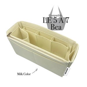 May include: A milk-colored bag organizer with multiple compartments and a zippered closure. The organizer is designed to fit inside a handbag and features the text "Compatible LE 5 A7 Bea" and "SILKON".