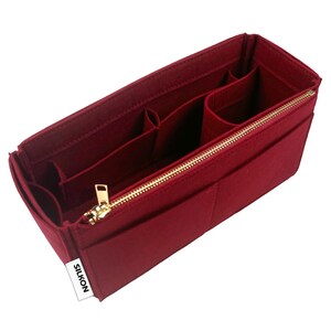 May include: A burgundy felt handbag organizer with multiple compartments and a gold zipper closure. The organizer has several pockets of varying sizes and a small white tag that reads "SILKON".
