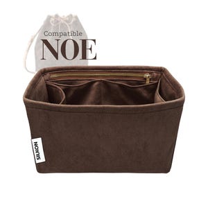 Puede incluir: Un organizador de bolso de fieltro marrón con múltiples compartimentos y un bolsillo con cremallera. El texto "Compatible NOE" se muestra encima del organizador, y la marca "SILKON" está en una etiqueta blanca en el lateral. Una bolsa con cordón está en el fondo.