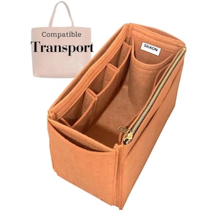 Peut inclure: Organisateur de sac en feutre orange avec plusieurs compartiments et une fermeture éclair dorée. L'organisateur est conçu pour s'adapter à l'intérieur d'un sac fourre-tout, comme le montre l'image avec le texte "Compatible Transport". La marque "SILKON" est visible.