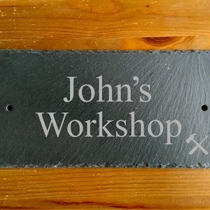 May include: Black slate sign with white text that reads "John's Workshop" and a small hammer and chisel symbol.