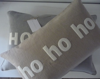 Puede incluir: Dos cojines rectangulares, uno gris claro, otro beige. Ambos cojines tienen las palabras "ho ho ho" y "ho" cosidas en blanco. Una etiqueta está sujeta al cojín gris.