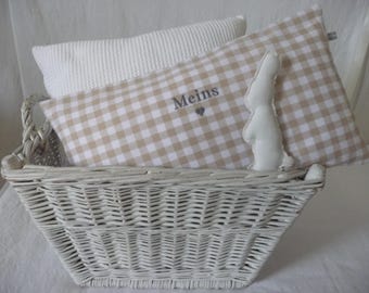 May include: A white wicker basket with two pillows inside. The pillows are beige and white gingham with the word "Meins" embroidered on one of them. One of the pillows has a white bunny shape sewn on it.