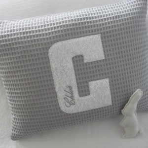 Cojín de piqué gofre con letras de rizo y nombre bordado en rosa viejo, gris claro, verde polvoriento y blanco.