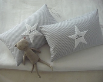 May include: Two gray and white striped pillow covers with white embroidered stars. The stars have the names "Lola" and "Lina" embroidered on them. A gray stuffed animal is lying on the pillows.