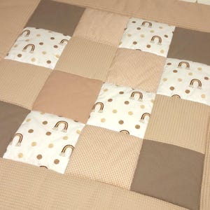 Könnte beinhalten: Eine Patchwork-Spielmatte mit verschiedenen Texturen und Mustern, darunter Braun, Beige und Weiß mit Regenbogen-Designs. Die Spielmatte ist aus weichem, bequemem Stoff gefertigt und perfekt für Babys und Kleinkinder.