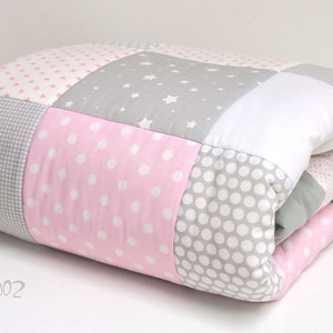 Könnte beinhalten: Eine rosafarbene und graue Patchwork-Decke mit verschiedenen Mustern, darunter Sterne, Punkte und Karos.