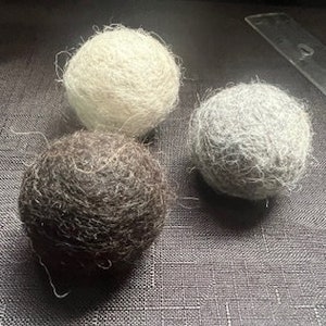 May include: Three wool dryer balls in different colors: dark brown, light gray, and off-white.