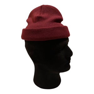 May include: A burgundy beanie hat made of soft knit fabric. The hat is folded down at the brim, creating a casual and comfortable look.