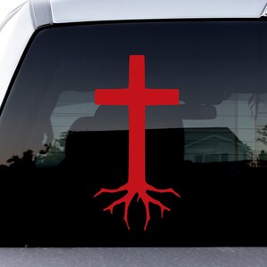 May include: A red cross with roots, a Christian symbol, is displayed on the back window of a silver pickup truck.