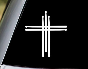 May include: A white vinyl sticker of a cross made of drumsticks. The sticker is on the back window of a car.