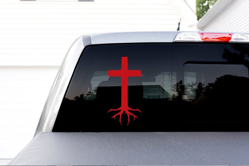 May include: A red cross with roots, a Christian symbol, is displayed on the back window of a silver pickup truck.