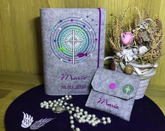 May include: A gray felt book cover with a colorful embroidered cross and the name "Marie" and the date "16.05.2020". A smaller gray felt pouch with a pink button and the name "Marie" is also shown.