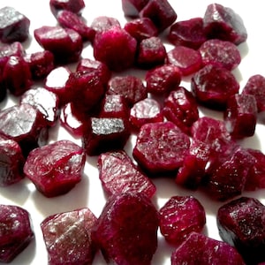 Puede incluir: Una colección de piedras preciosas de rubí en bruto. Los rubíes son de color rojo intenso y tienen una variedad de formas y tamaños.