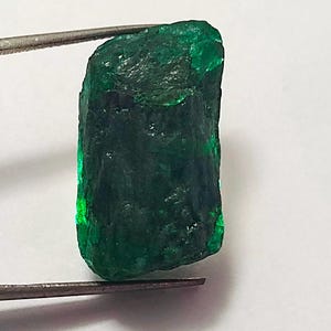 May include: A large, rough, emerald green gemstone with a rectangular shape.