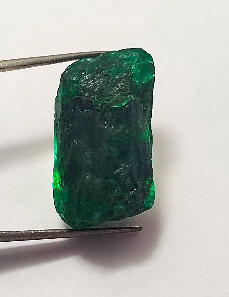 May include: A large, rough, emerald green gemstone with a rectangular shape.