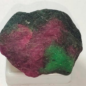 Peut inclure: Une pierre précieuse brute de forme irrégulière avec un mélange de couleurs vertes, roses et noires. La pierre précieuse a une apparence naturelle et non polie.